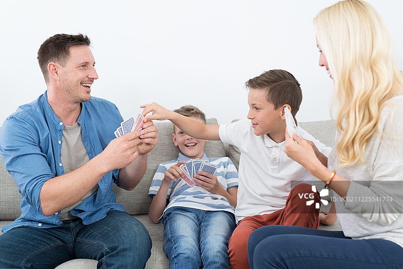 快乐的年轻家庭在家里玩纸牌游戏。图片素材