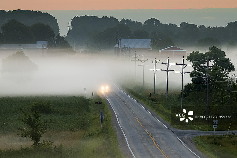远处的汽车行驶在道路上的雾在日出，圣安娜，威斯康星州，美国图片素材