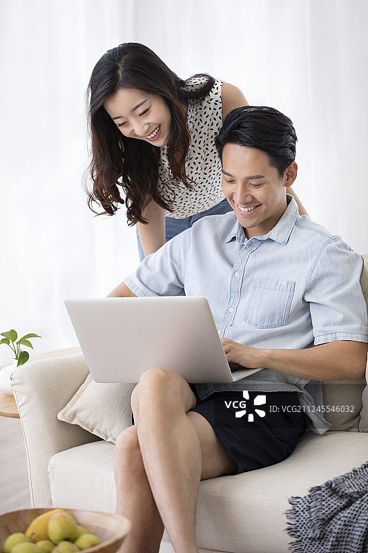 快乐的年轻情侣在客厅使用笔记本电脑图片素材