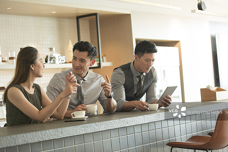 一对成功青年商务男女喝咖啡聊天和另一个商务男士使用平板电脑工作在公司茶水间图片素材