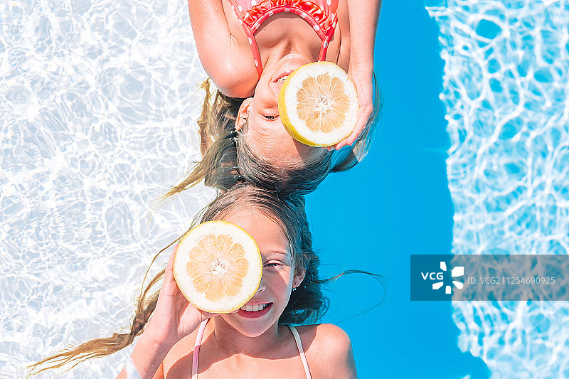 夏天，两个女孩捧着柠檬在游泳池里浮在水面上图片素材