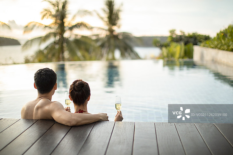 快乐的年轻情侣在泳池边喝香槟图片素材