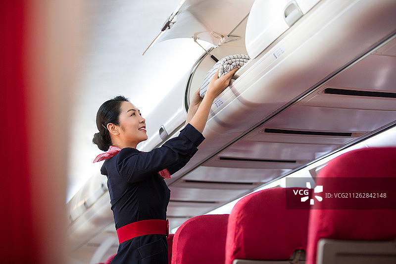 青年女乘务员在飞机机舱工作拿着毯子放入行李架内图片素材