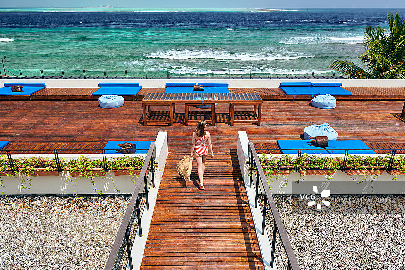 女人在红色条纹泳衣走在热带海滩露台甲板。暑假在马尔代夫。图片素材