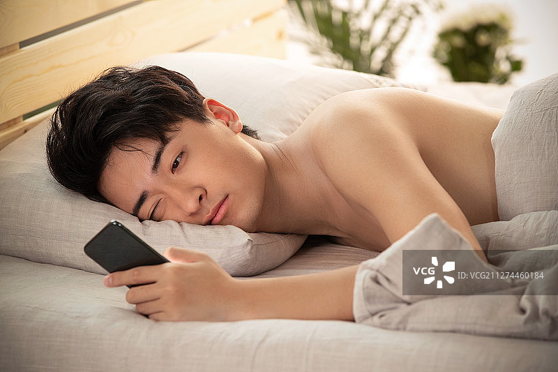 躺在床上玩手机的年轻男人图片素材
