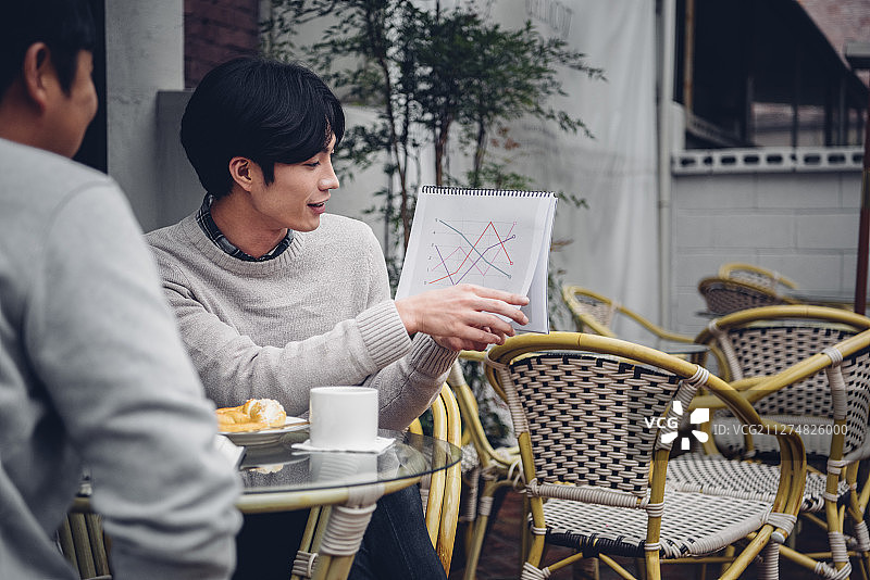 两个男人坐在桌子旁吃早午餐的照片在café户外一起看图表图片素材