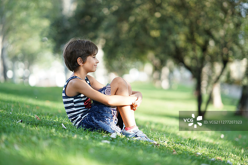 一个八岁的小女孩，坐在城市公园的草地上小女孩，八岁，坐在户外的草地上。图片素材