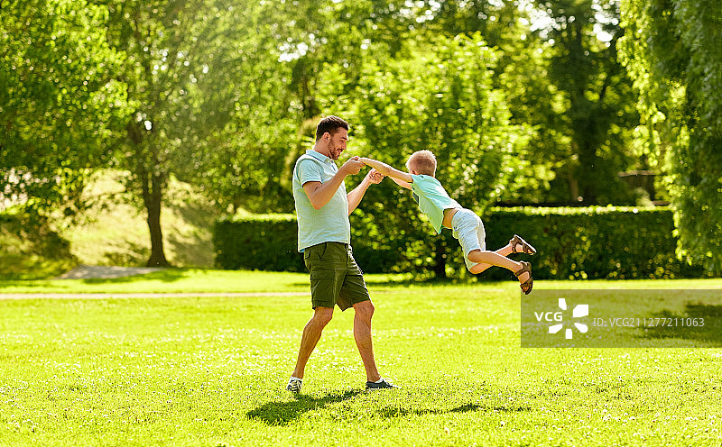 家庭、休闲、人的概念——快乐的父亲和小儿子在夏日公园玩耍。快乐的父亲和儿子在夏季公园玩图片素材