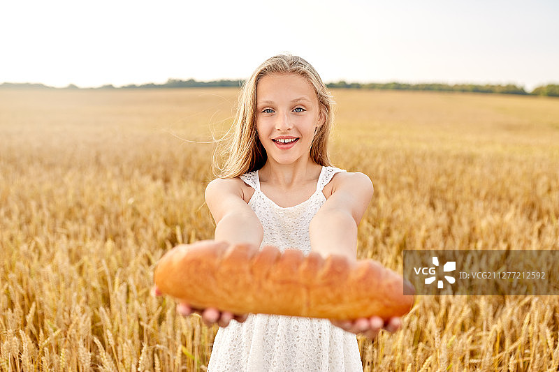 自然，健康的饮食和收获的概念-微笑的年轻女孩拿着一条白面包在谷物田在夏天。在谷物地里拿着白面包的女孩图片素材