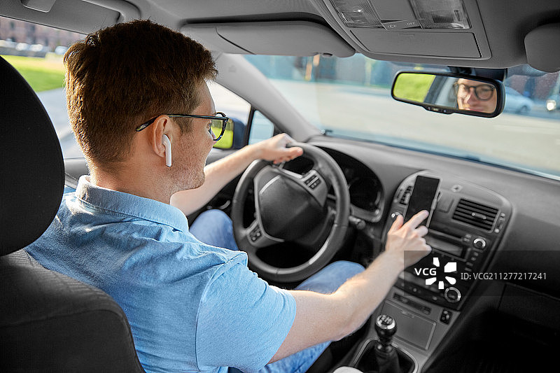 交通，车辆和人的概念-人或司机与无线耳机驾驶汽车和使用智能手机上的GPS导航。男人在开车，用智能手机上的GPS图片素材