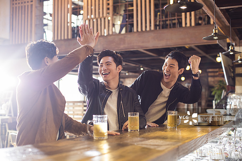 快乐的年轻男士在酒吧喝酒欢呼图片素材