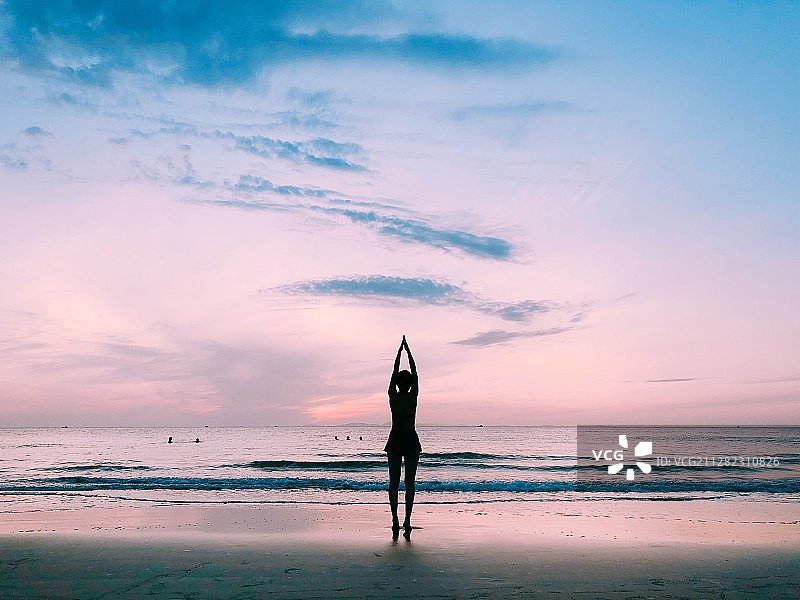 女性瑜伽练习者站在沙滩上举起手臂的剪影图片素材