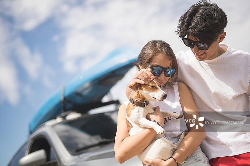 一对夫妇抱着小狗倚靠在停在沙滩上的汽车上图片素材