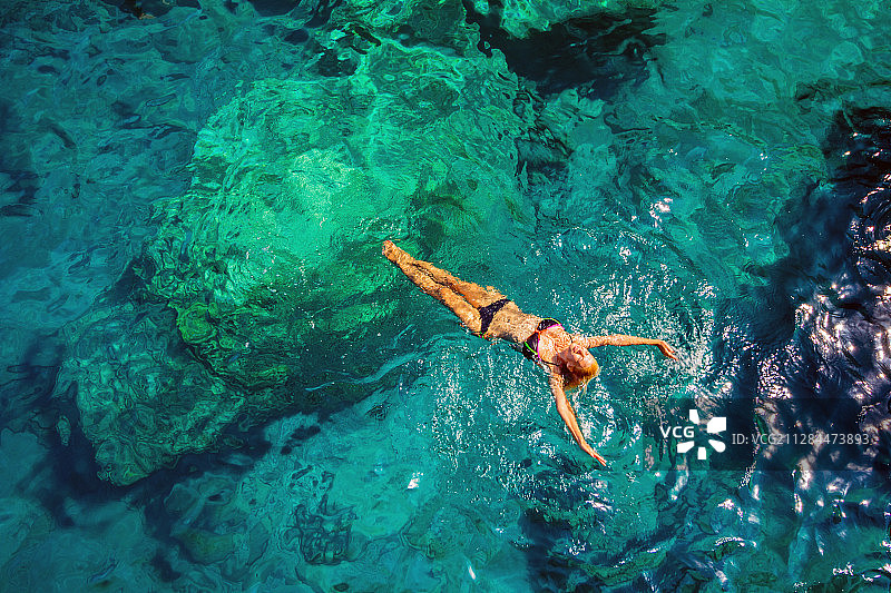 高角度的金发女子游泳在透明的翡翠水，Beykonak，土耳其图片素材