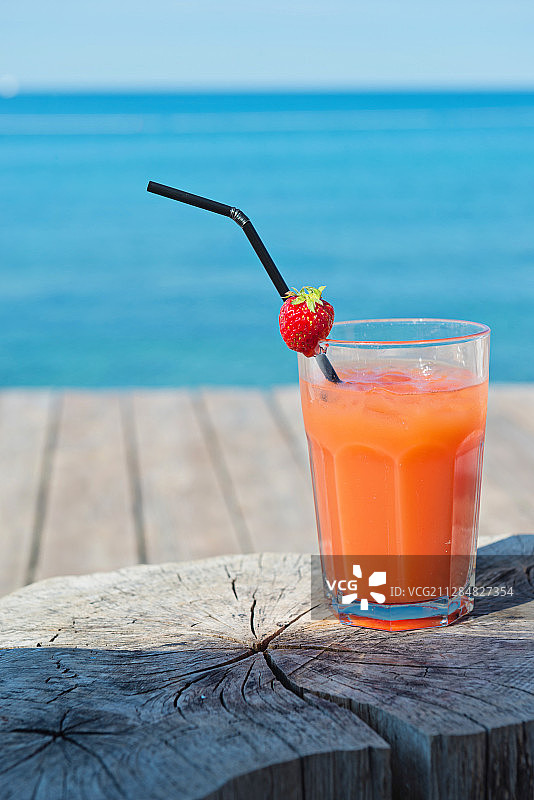 海滨码头上的树桩桌上放着一杯橙色的鸡尾酒图片素材