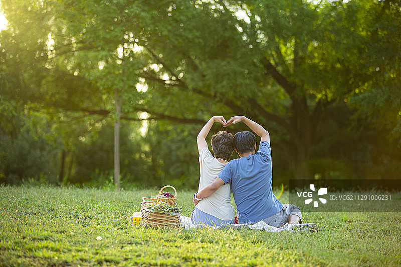 夕阳下老年夫妻在户外公园野餐做心型手势图片素材