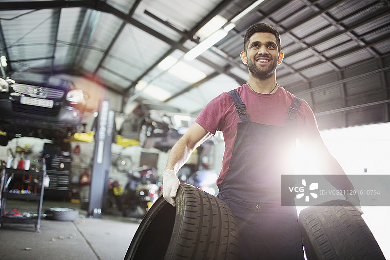 肖像微笑的男性技工携带轮胎在汽车修理店图片素材
