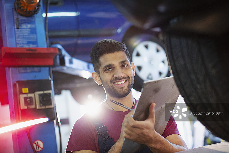 肖像自信，微笑的男性技工与剪贴板在汽车修理店图片素材