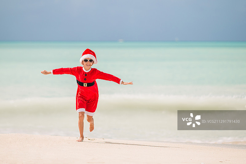 可爱的小女孩戴着圣诞帽在热带海滩上图片素材