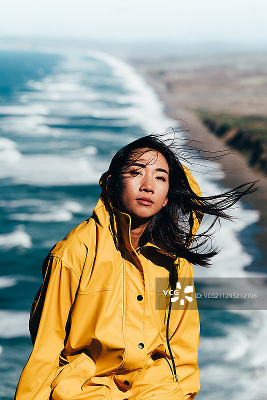 美国因弗内斯，一名身穿黄色雨衣的年轻亚洲女子对着大海的肖像图片素材