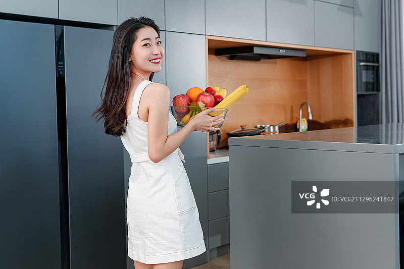 拿着水果的青年女人站在冰箱前图片素材