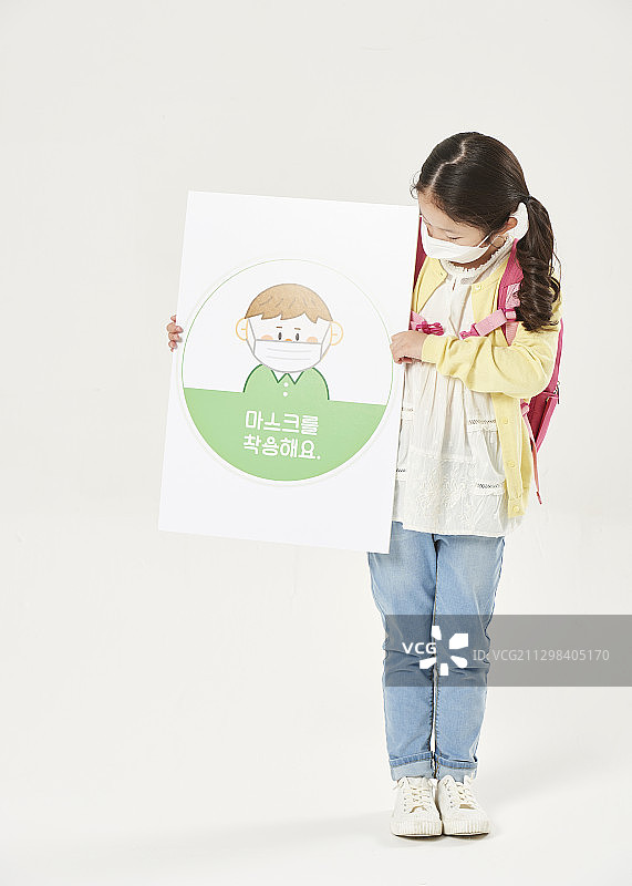 小学女孩戴着污染口罩站着举着安全规则的标志图片素材
