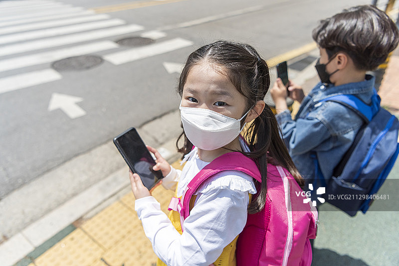 男孩和女孩戴着防污染口罩在人行横道旁看智能手机图片素材