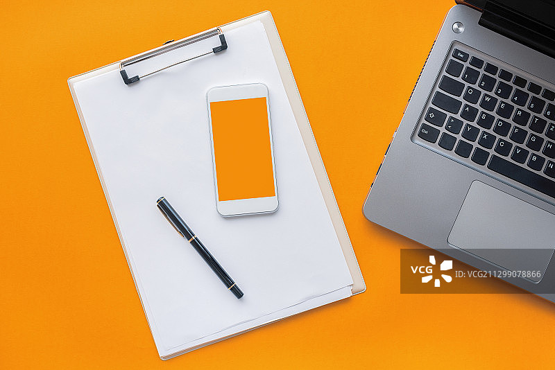 上面直接拍摄的剪贴板与移动电话和剪贴板的笔记本电脑在橙色背景，诺维萨德，塞尔维亚图片素材