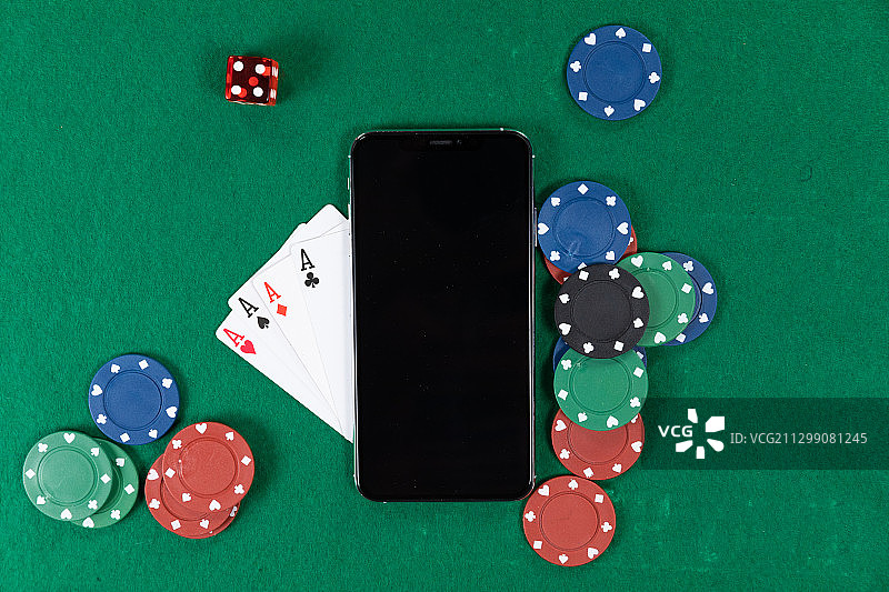 画面中是黑色的智能手机、扑克牌、红色的骰子和纯绿色表面上的彩色代币图片素材