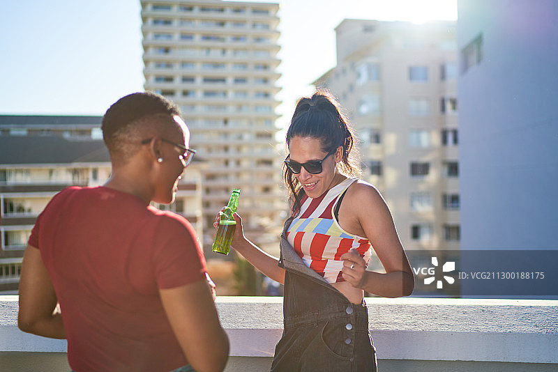 无忧无虑的年轻女子跳舞和喝啤酒在阳光明媚的城市屋顶图片素材