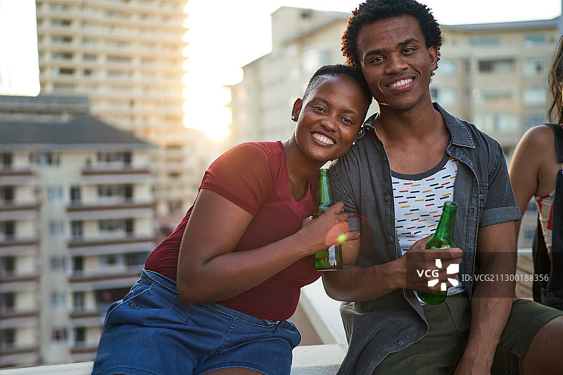 肖像快乐的年轻夫妇在城市的屋顶上喝啤酒图片素材