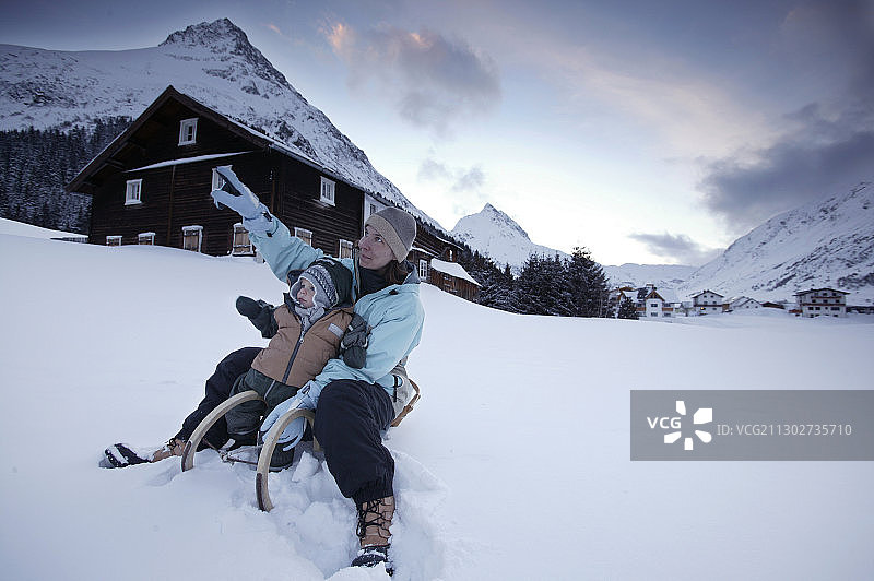 奥地利蒂罗尔的加尔图尔，一个女人和一个孩子坐在雪橇上，背景是戈芬斯皮策和巴伦斯皮策图片素材
