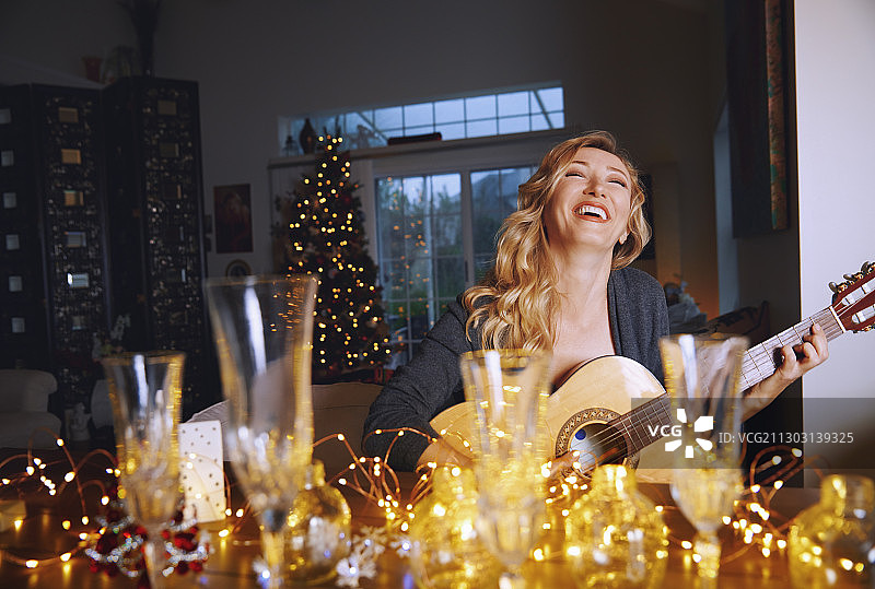 笑着的女人坐在圣诞桌旁弹吉他图片素材