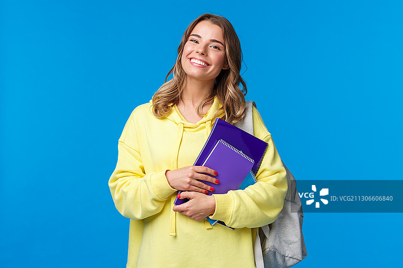 一个微笑的年轻女人的肖像拿着学校的书和背包对蓝色的背景图片素材