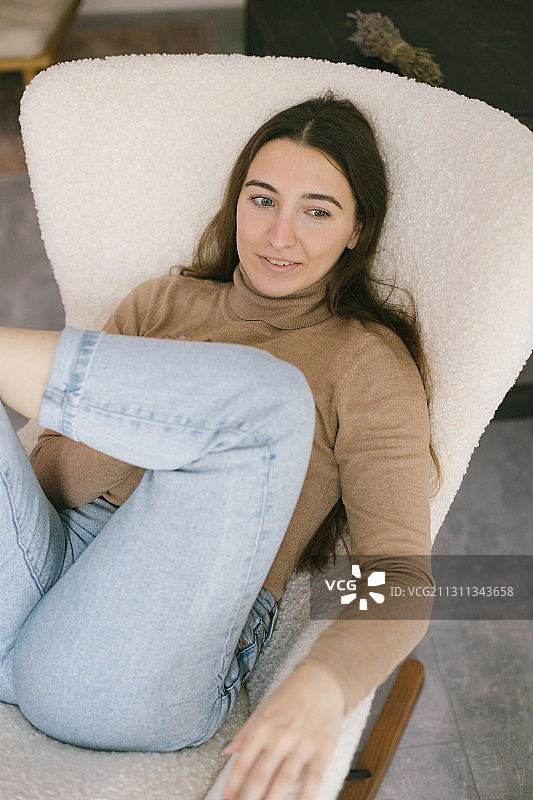 年轻女子放松在舒适的白色椅子在家里，俄罗斯图片素材