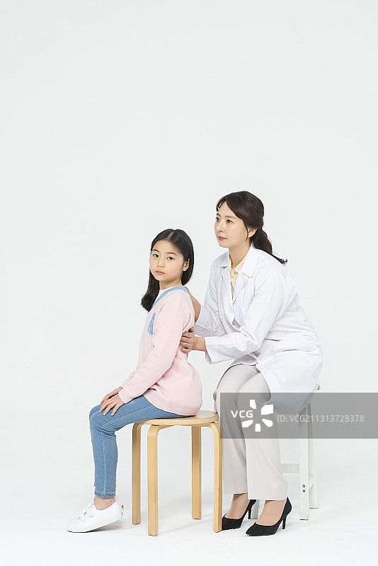 医生坐在白色背景的椅子上检查女孩的脊柱图片素材