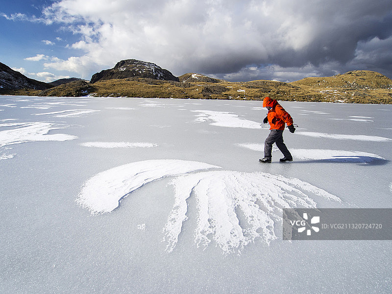 英国坎布里亚湖区，一名登山者在博罗代尔山头的洒水塔恩上，被冻住了，看着伟大的尽头，积雪在冰上形成了图案。图片素材