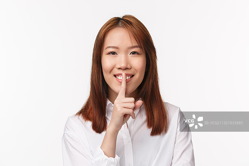 微笑的年轻女子的肖像与手指在嘴唇上的白色背景图片素材