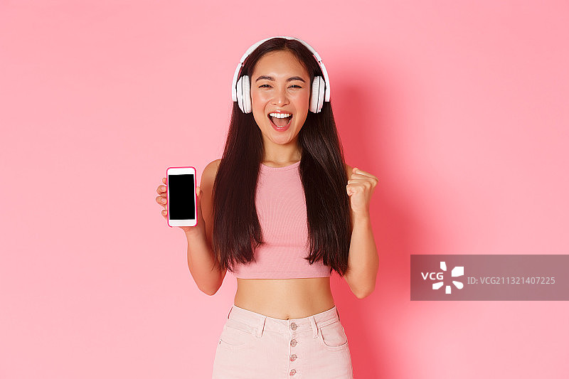 照片中的年轻女子戴着耳机，手持手机，背景是粉色图片素材