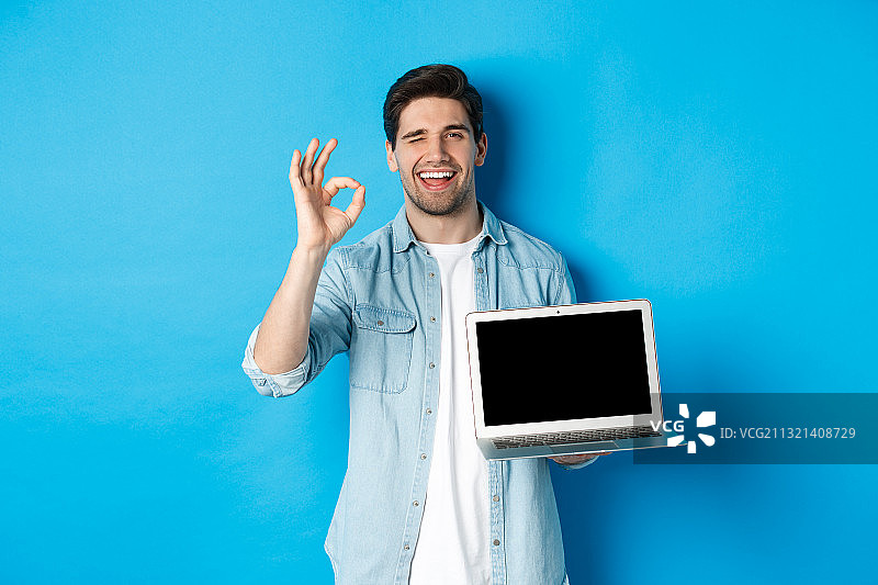 一名微笑的男子拿着平板电脑，背靠蓝色墙壁图片素材