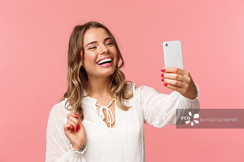 粉色背景下微笑的女人拿着手机的肖像图片素材