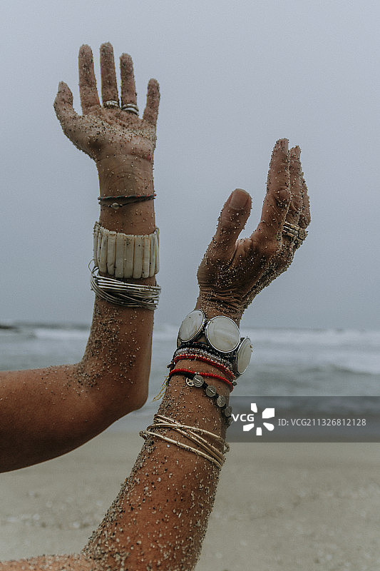 裁剪照片的两个沙涂层和珠宝覆盖的女性手臂在海滩，秘鲁图片素材