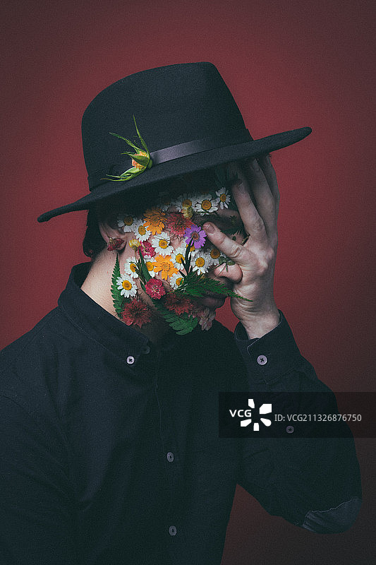 特写男子戴着帽子和花卉面具的红色背景，巴黎，法国图片素材