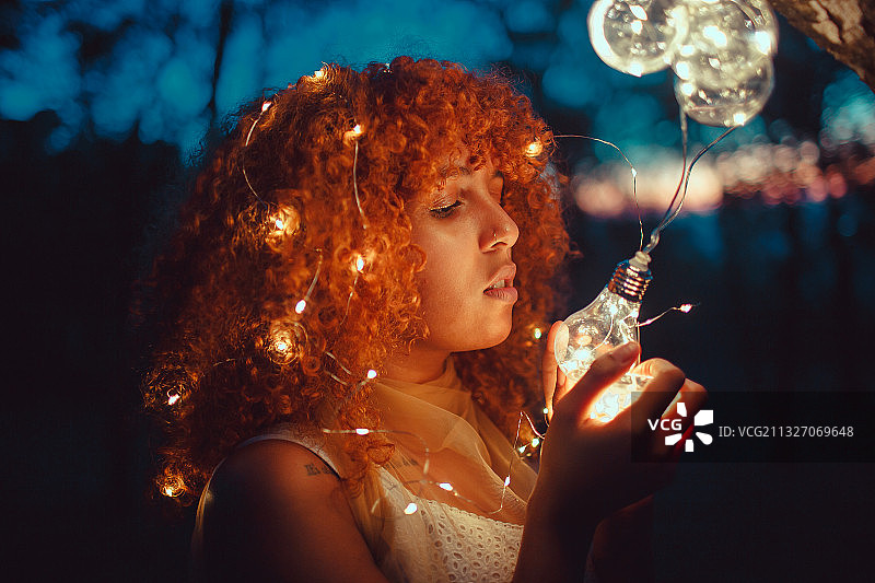 年轻女子的颜色与红色头发和stringlights在晚上，贝洛奥里藏特，米纳斯吉拉斯州，巴西图片素材