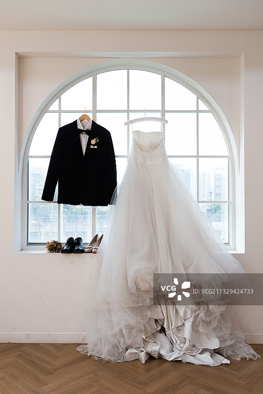 一件燕尾服和一件婚纱挂在窗前的衣架上图片素材