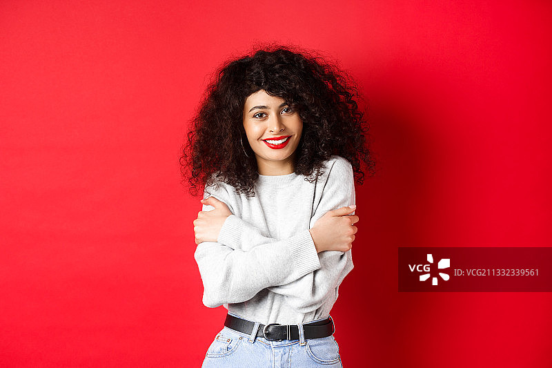 微笑的年轻女子的肖像双臂交叉站在红色的背景图片素材