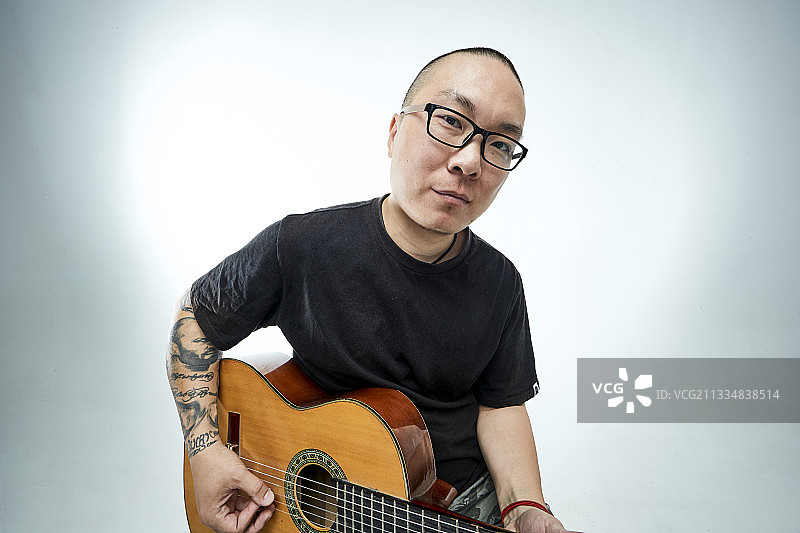 示范演奏古典吉他的亚洲男性乐手人像图片素材