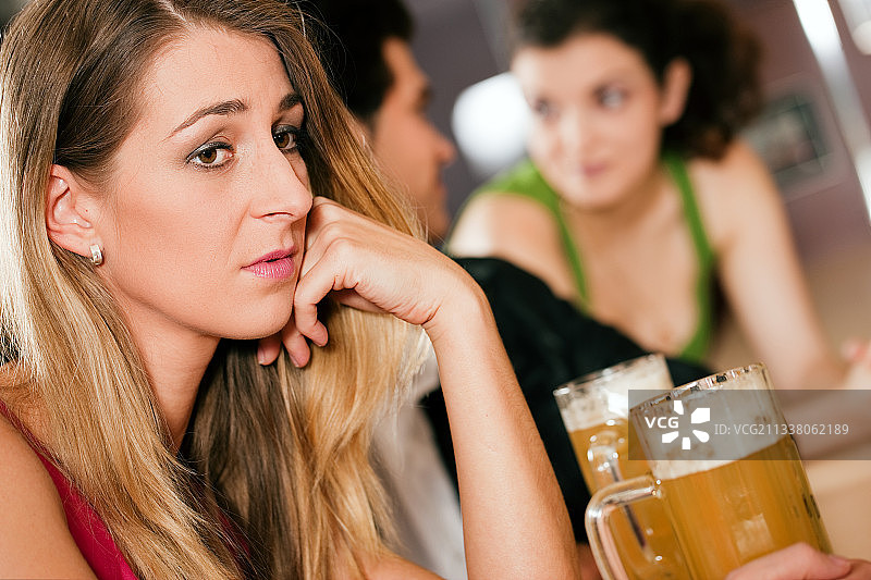 一群人在酒吧或餐馆喝啤酒，女人在前面伤心，因为她的男朋友和另一个女孩调情甩了她图片素材
