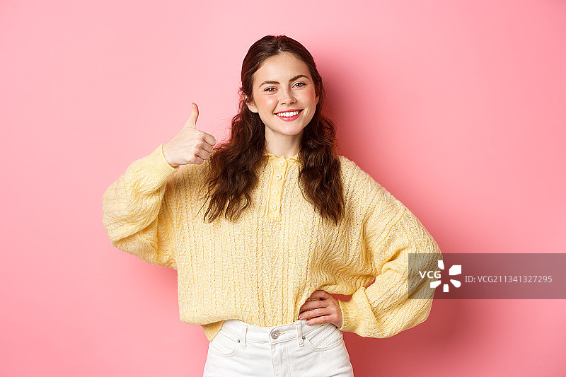 微笑的年轻女子肖像在粉红色的背景下做手势图片素材
