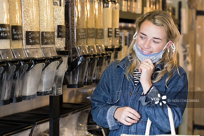 英国，年轻的金发女子戴着口罩，在免费垃圾食品商店购物。图片素材